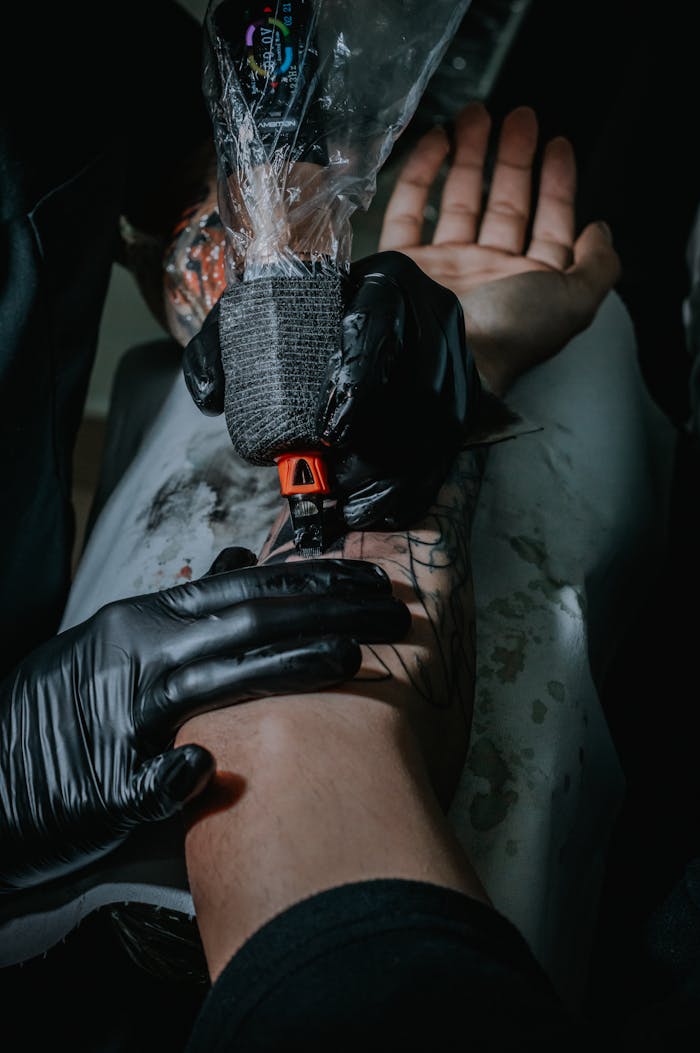 Tattoo artist working meticulously on a clients arm tattoo. Close-up of the tattoo process with gloves and tattoo machine.
